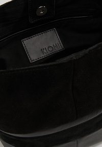 Wnętrze czarnej torby z wytłoczoną skórzaną etykietą z napisem "KIOMI", miękką teksturą zamszu i prostym wzorem z zapięciem na zatrzask.