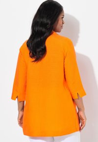 Oranje linnen tuniek met driekwart mouwen, zijopeningen en een losse pasvorm. Heeft een gladde textuur en een eenvoudige, strakke ontwerp.