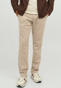 Pantalones de chándal beige con una textura suave y un diseño entallado, combinados con zapatillas blancas que tienen detalles en rojo y negro.
