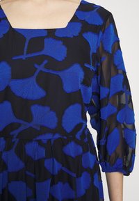 Vestido preto com bordado de folhas de ginkgo azuis. Apresenta um decote quadrado e mangas bufantes três quartos, feito de um tecido leve e translúcido.