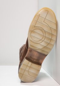 Zapato de ante marrón con suela de goma texturizada, que presenta un logo circular y acentos cosidos a lo largo del costado. Talla 41 indicada en la suela.