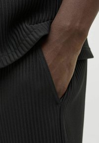 Black ribbed fabric features a close-up view of a pocket detail, showcasing soft texture and clean seams against a skin tone background.