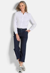 Chemise blanche à boutons avec manches longues, associée à un jean droit bleu marine et des baskets grises, offrant un look décontracté et soigné.