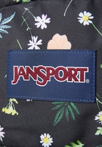 Jansport kuprinė, pagaminta iš tamsaus audinio su rožių raštu, kuriame dominuoja rožinė, geltona ir balta spalvos. Įeina jūros mėlynumo etiketė su balta ir bordo logo.