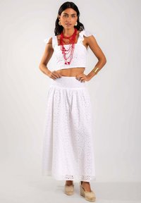Conjunto de top corto de ojo de perdiz blanco y falda larga, con patrones florales, tela texturada y collar rojo en capas. Modelo lleva sandalias de cuña.