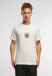 Off-white bomullströja med rund hals och korta ärmar, prydd med en svart örn emblemet och texten "BUNDESWEHR" på bröstet.