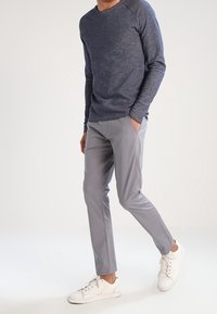 Marinblå långärmad tröja med rundad halsringning, grå slim-fit byxor och vita sneakers. Slät textur och subtil färgkontrast.