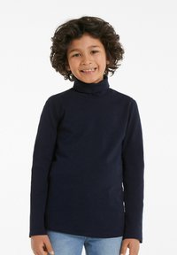 Navyblaues Rollkragenoberteil aus weichem Stoff, mit langen Ärmeln und tailliertem Schnitt. Getragen mit hellblauen Denim-Jeans.