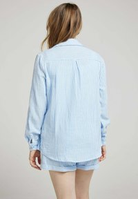 Chemise à rayures bleu clair et blanche, à boutons, avec de longues manches et un ourlet arrondi, associée à un short assorti présentant des rayures similaires.