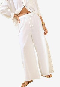 Pantalons larges blancs en tissu léger, dotés d'une taille élastique et d'une broderie latérale avec des accents dorés.