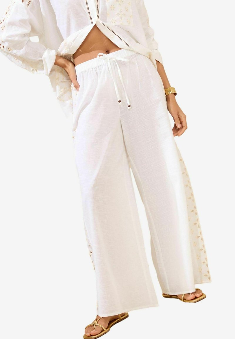Pantalons larges blancs en tissu léger, dotés d'une taille élastique et d'une broderie latérale avec des accents dorés.
