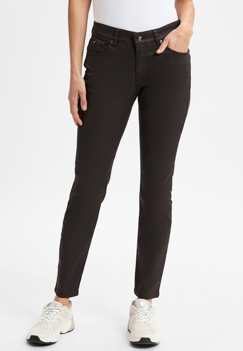 Zwarte slim-fit broek van een katoenmix. Heeft voorzakken en een metalen knoopsluiting. Gecombineerd met lichtgekleurde sneakers.