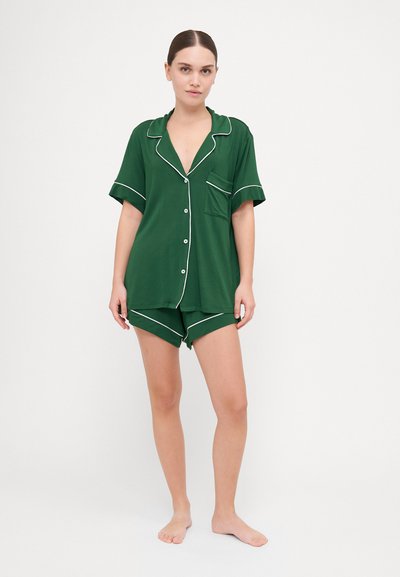 Conjunto de pijama verde de manga curta com acabamentos brancos, composto por uma camisa de botão e calções a condizer. Textura suave, corte descontraído e detalhe de bolso.