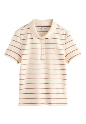 Kvinde med flettet hår iført en beige kortærmet polo med brune vandrette striber og taupe bukser mod en lys baggrund.