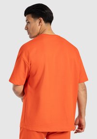 Pánské tričko s krátkým rukávem v jasně oranžové barvě, vyrobené z měkké tkaniny. Má uvolněný střih a jednoduchý design s kulatým výstřihem.