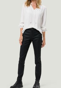 Blouse blanche à manches longues avec des poignets retroussés, associée à un pantalon noir ajusté et des bottes à la cheville. Design minimaliste avec des lignes épurées et des couleurs neutres.