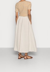 Gestreepte bruine en crèmekleurige top met korte mouwen, gecombineerd met een lange, vloeiende crèmekleurige rok; bruine sandalen met banden; het kledingstuk heeft een relaxed silhouet.