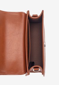 Sac à main en cuir marron ouvert à plat montrant un grand compartiment intérieur avec une poche plaquée et une fermeture argentée.