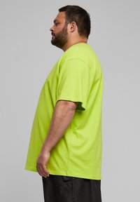 T-shirt di cotone verde neon con maniche corte, colletto a girocollo e vestibilità morbida, mostrata da un'angolazione laterale.