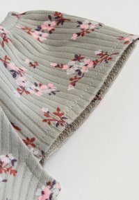 Rebrasta siva tkanina z rožnim vzorcem v roza, beli in vijolični barvi, prikazana bližinsko na šiv rokava oblačila na belem ozadju.