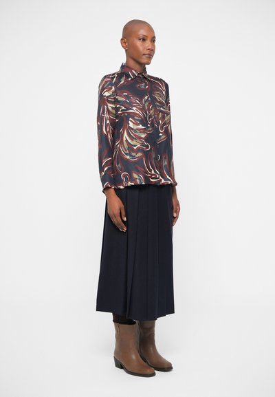 Mønstret langærmet skjorte i marineblå med svulst af creme og burgunder; parret med en plisseret marineblå nederdel og brune ankelstøvler.