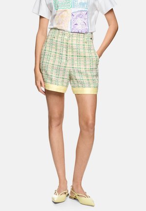 Person wearing yellow and green plaid tailored shorts with a cuffed hem, paired with pale yellow slingback flats and a colorful graphic t-shirt.