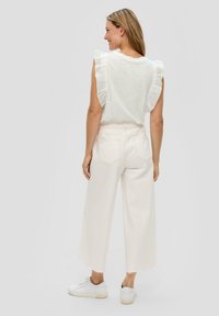 Biała, marszczona bluzka bez rękawów zestawiona z białymi spodniami o szerokim kroju i wysokim stanem. Model nosi białe sneakersy. Z tyłu schludne kieszenie w spodniach.