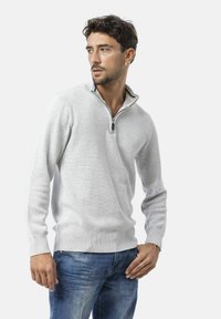 Hellgrauer Pullover mit Reißverschlusskragen, gerippten Bündchen und Saum, aus einem gestrickten Stoff. Getragen mit blauen Jeans.