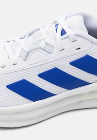 White athletic shoe featuring blue textured stripes, mesh upper, padded collar, and a lightweight rubber sole.