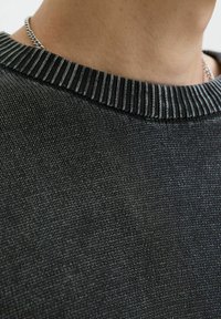 Czarny sweter dzianinowy o fakturowanym wykończeniu i prążkowanym kołnierzem, z naprzemiennymi ciemnymi i jasnymi paskami. Zbliżenie.