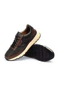 Zapatilla marrón y negra con materiales de malla y cuero, punta redondeada, suela texturizada y costura decorativa en el lateral.