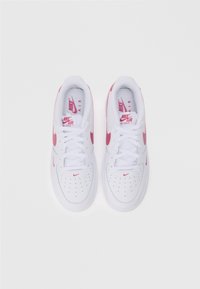 Nike Air Force 1 tennarit valkoisesta nahasta, jossa on vaaleanpunaisia yksityiskohtia. Pyöreä kärki, nauhakiinnitys, rei'itetyt sivut ja tunnusomaiset logo-yksityiskohdat.