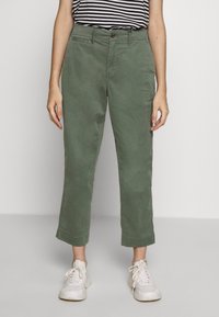 Zelené bavlněné kalhoty s rovnými nohavicemi, s manžetami, s jedním knoflíkem a předními kapsami, doplněné o bílé tenisky.