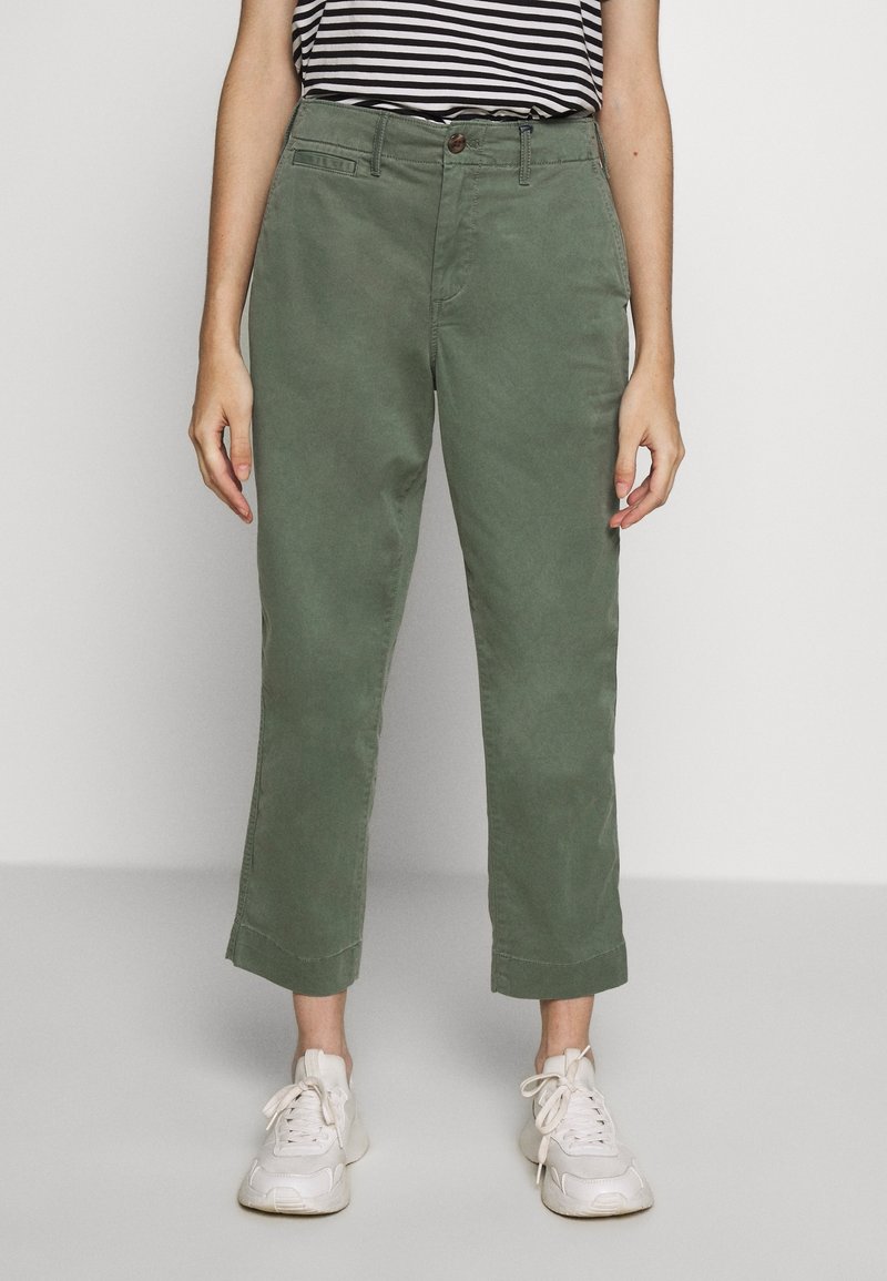 Zelené bavlněné kalhoty s rovnými nohavicemi, s manžetami, s jedním knoflíkem a předními kapsami, doplněné o bílé tenisky.