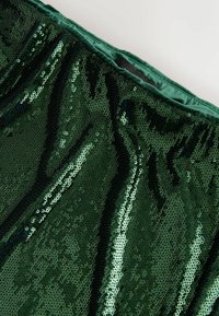 Grüner Paillettestoff mit glatter Textur und einer glänzenden, reflektierenden Oberfläche. Bündchen aus dunklerem grünen Satin gefüttert.
