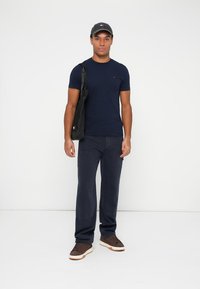 Námornícky tričko, tmavé nohavice a hnedé tenisky. Čierna taška prehodená cez rameno. Sivá čiapka s logom. Jednoduchý, ležérny dizajn s jednoliatymi farbami.