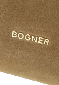 Materiale in suede marrone con logo "BOGNER" in rilievo in oro, texture liscia con finitura opaca, forma rettangolare, design minimalista.