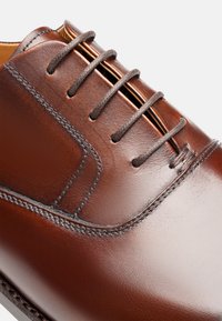 Braune Lederdressschuhe mit glatter Textur, runder Zehenform und sechslöchrigem Schnürsystem mit dekorativem Stichdetail.