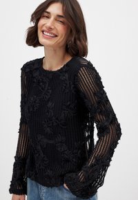 Schwarzes Langarmshirt mit floraler Stickerei, aus strukturiertem Stoff. Mit Rundhalsausschnitt und filigranem Muster an den Ärmeln.