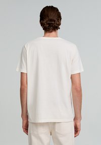 Cremefarvet bomulds t-shirt med klassisk rund halsudskæring og korte ærmer, med et lille mærkeskilt nær sømmen.