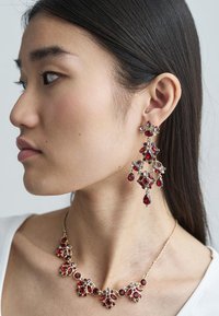 Røde juveløredobber og matchende halskjede har gullaccentuer, intrikate design og varierende edelsteinformer, inkludert runde og dråpeformede fasetter.