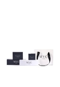 Quatre boîtes d'emballage en noir et blanc avec le logo "MYC PARIS", accompagnées d'un sac en papier blanc avec des poignées noires, sur un fond uni.