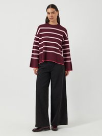Maglione a righe bordeaux con righe orizzontali rosa, maniche larghe e orlo corto, abbinato a pantaloni neri larghi e scarpe lucide.