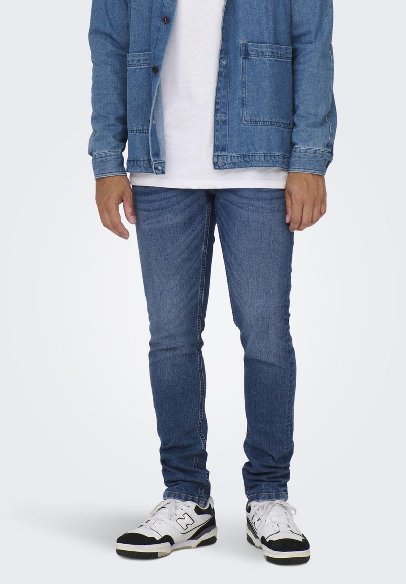 Jeans de mezclilla azul claro con un corte ajustado, que cuentan con bolsillos delanteros y traseros. Combinados con una camiseta blanca y zapatillas en blanco y negro.