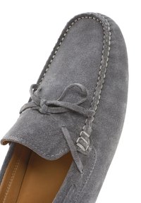 Zapato moccasín de ante gris con costura decorativa y un detalle de lazo en la parte delantera. El interior presenta un forro beige y una textura suave.