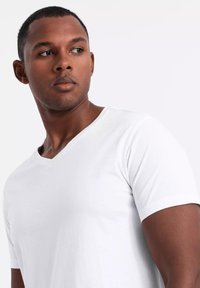 Camiseta blanca de manga corta y escote en V, hecha de tela suave, con un diseño ajustado y costuras mínimas, que muestra un contorno limpio y simple.