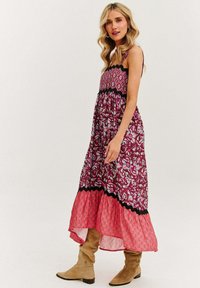 Maxi sukienka z dopasowanym burgundowym topem, czarną koronkową lamówką i rozkloszowanym, warstwowym dołem w różowe kwiatowe wzory, w połączeniu z beżowymi botkami do kolan.