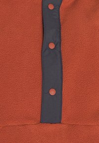 Tessuto di pile rosso con un pannello blu scuro che presenta tre bottoni rossi tondi lungo il centro. Texture morbida con un aspetto caldo.