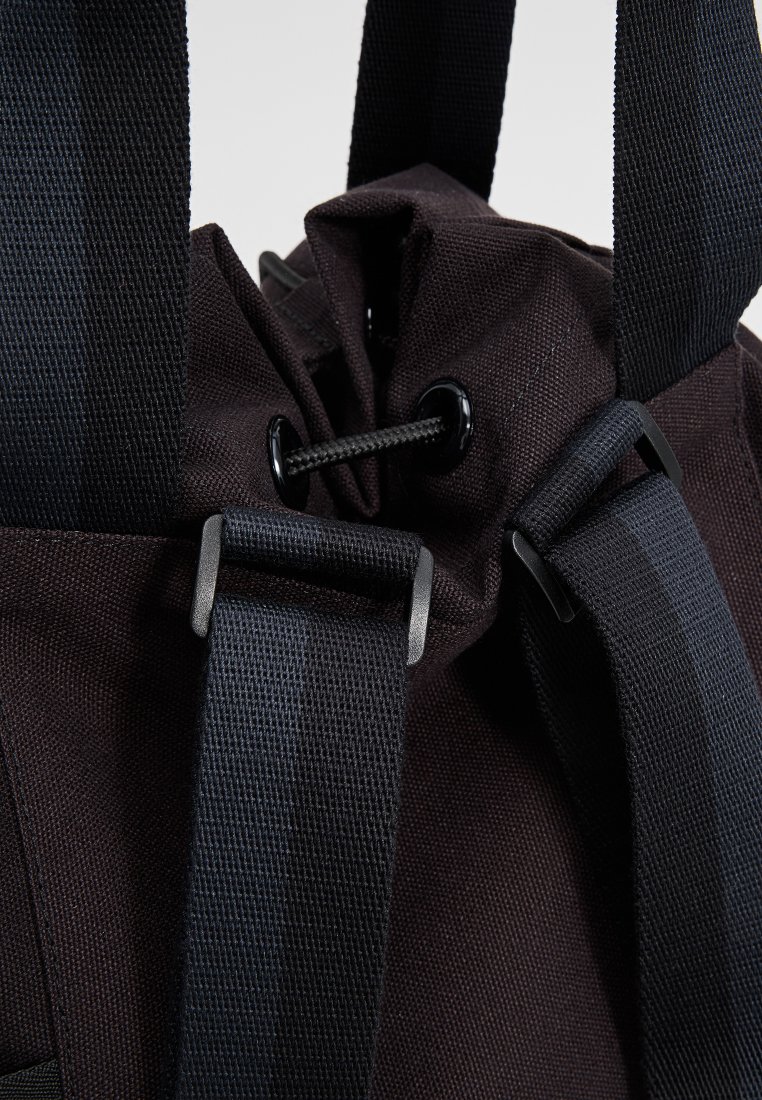 Bolsa de tela negra con cierre de cordón, que cuenta con correas negras duraderas y acentos de metal, mostrando una superficie texturizada.