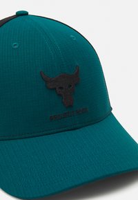 Teal cap med et sort tyrelogo og "PROJECT ROCK" tekst. Har tekstureret stof og en buet skygge. Sorte accenter omkring kronen.